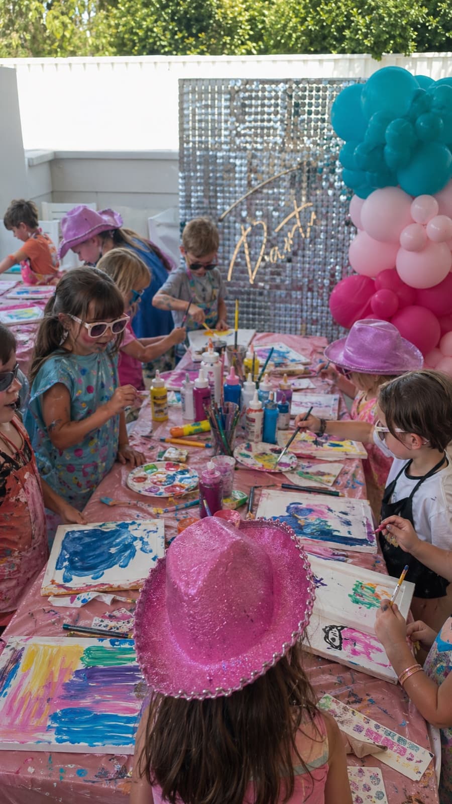 Kids in pink cowboy hats painting wood-frame canvases at an outdoor pink-themed party
