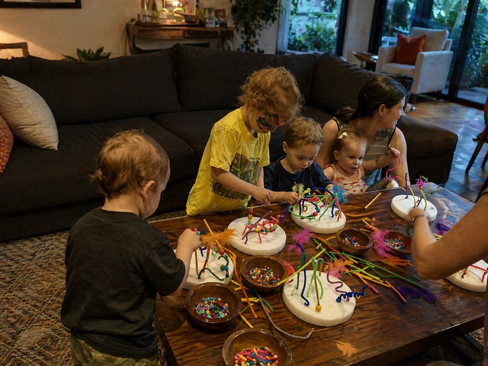Toddlers and parents making colorful dreamcatcher feather crafts on a living room coffee table