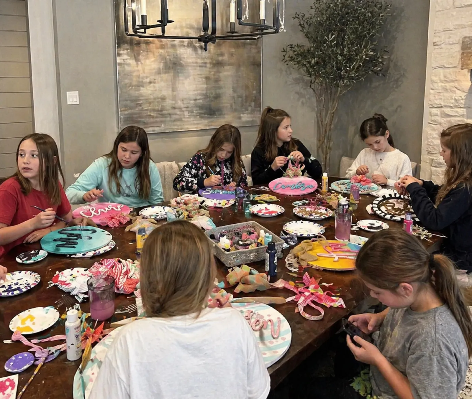 Older kids focused on painting personalized name plaques at a dining table