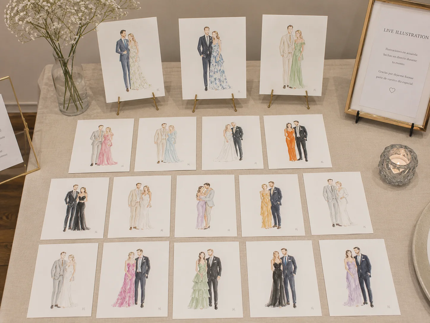 The live illustration display table at a wedding reception, with finished watercolor guest portraits on gold easels and laid out in rows for guests to collect