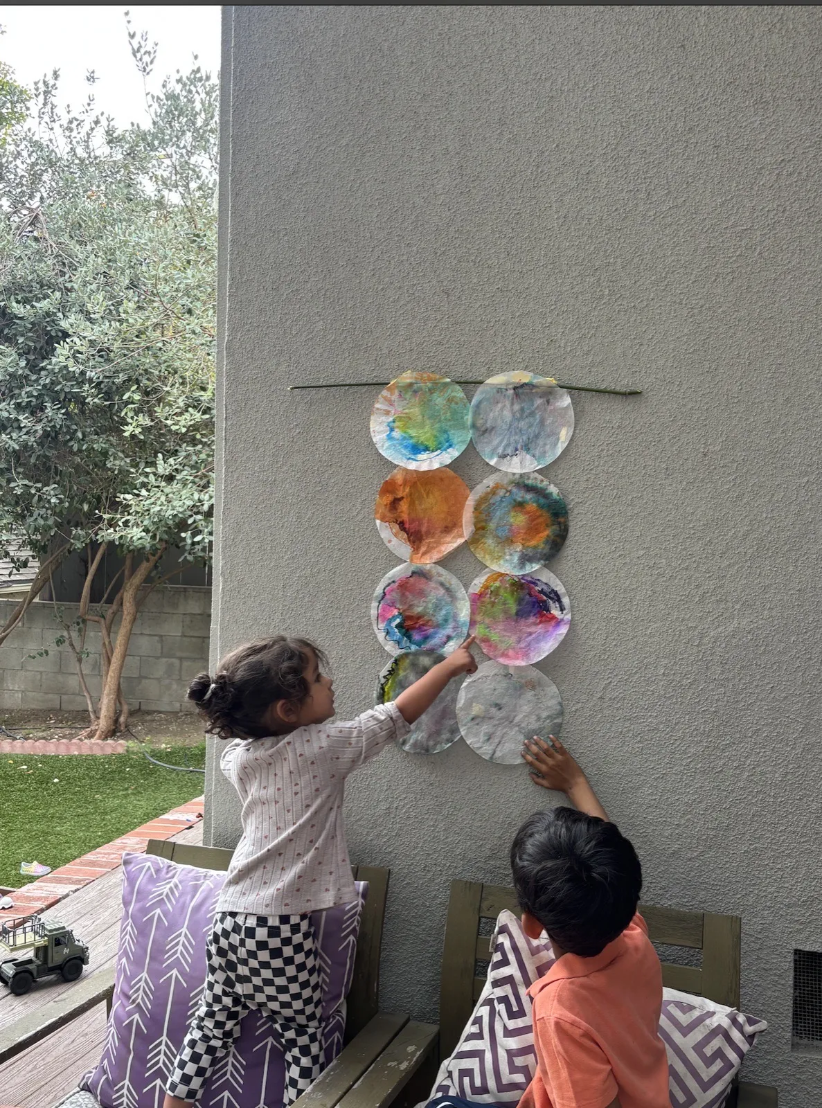 Two kids hanging colorful coffee-filter paintings on an outdoor wall